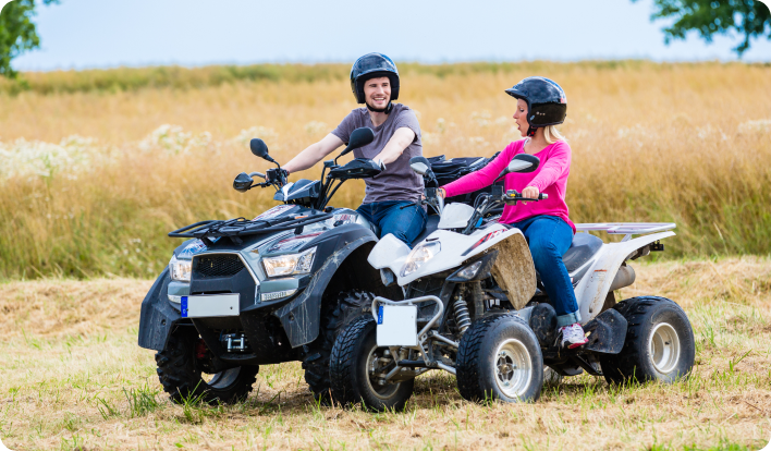 A couple sitting on their ATVs in a field